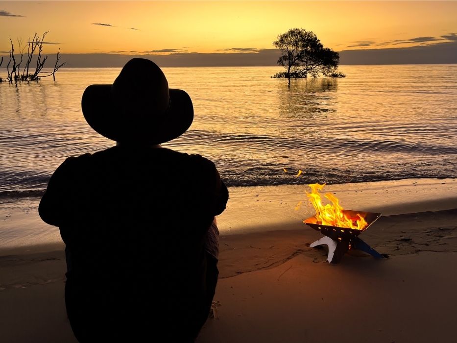 best fire pit for camping on beach with man sitting at sunset