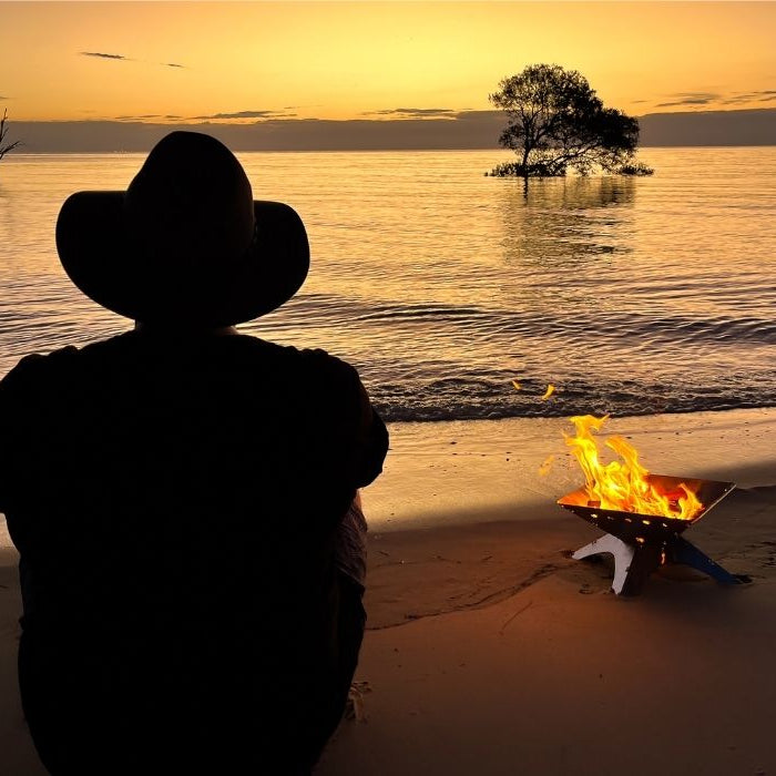 best fire pit for camping on beach with man sitting at sunset