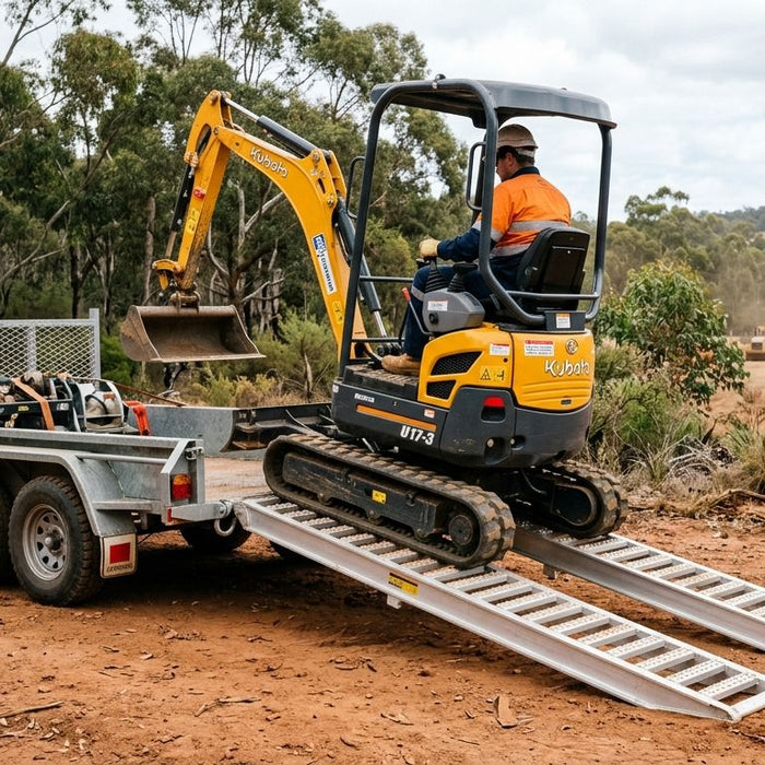 Mini excavator driving up a pair of aluminium loading ramps onto a trailer