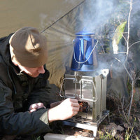 Man using Winnerwell Mini BBQ Smoker at riverside camp — 5-in-1 portable camping smoker at dusk